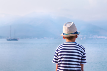 child in hat looking at sea and ship