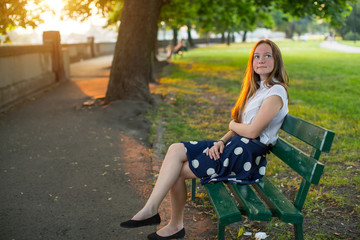 Cute young girl with long golden hair sitting alone on a bench in the Park.
