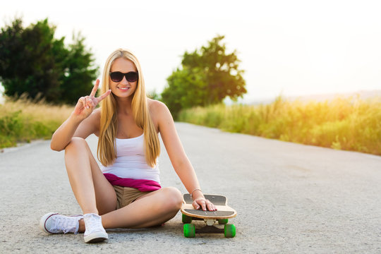 Attractive smiling hipster teenage girl with skateboard, image with sunflare