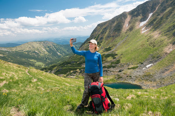 Woman hiker taking selfie with smartphone in the mountains