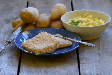 Coated cheese with homegrown peeled potatoes on wooden background