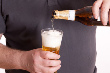 Mann gießt vor dem Bierbauch die Flasche Bier in ein Bierglas