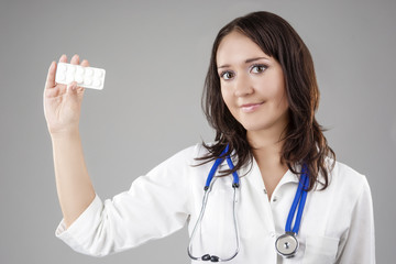 Medical Concept: Professional Female Caucasian Doctor Holding and Showing White Pills/Tablets Pack.Posing Against Gray