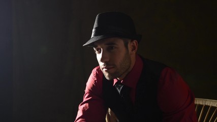 A man in a dark room tipping his hat with a gun
