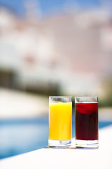 Two glasses of cherry and orange juice by the pool in summer