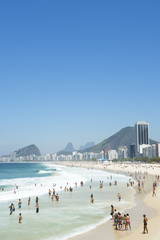 Obraz premium Beachgoers line the shore of Copacabana Beach on a bright summer morning in Rio de Janeiro, Brazil