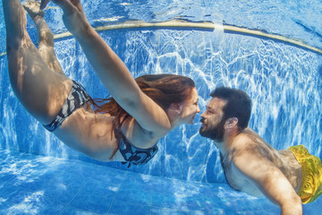 Happy newlywed family having fun on tropical honeymoon holidays -  positive couple swimming and diving underwater in outdoor pool. Healthy lifestyle and people water sports activity on summer vacation