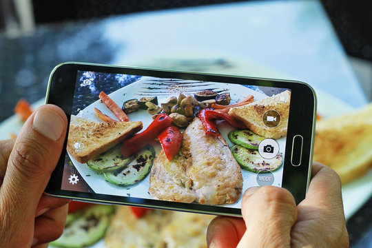 Male hands with smartphone taking photo of grilled chicken with