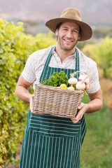 Young happy farmer holding a basket of vegetables