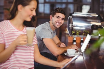 Smiling young man sitting at bar and using laptop 