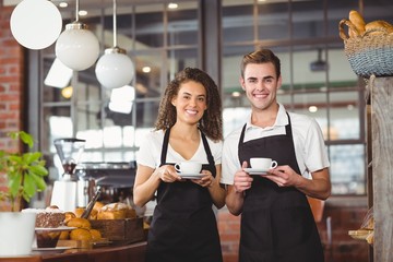 Smiling waiter and waitress holding cup of coffee - obrazy, fototapety, plakaty