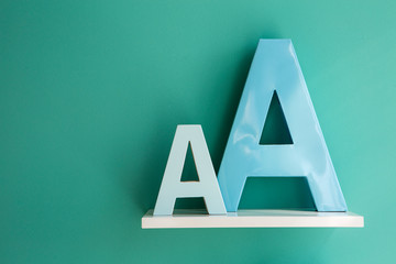 Letters A small and big size turquoise color on a white shelf.