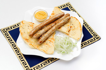 Dish with grilled sausages, pita bread, mustard and greens