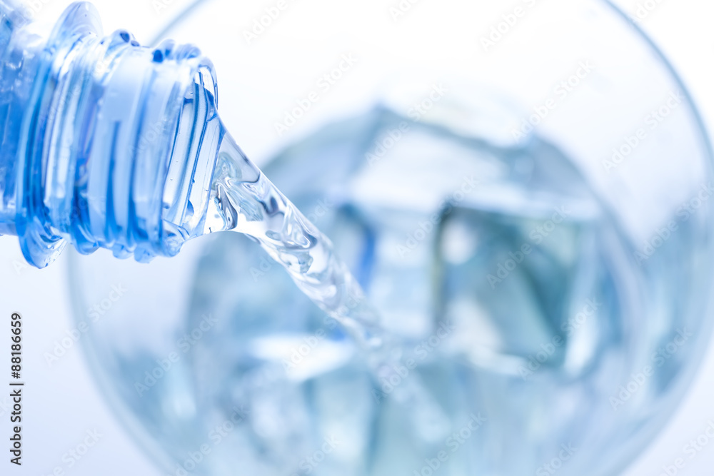 Wall mural pouring water in an elegant glass with ice and water drops. Macro