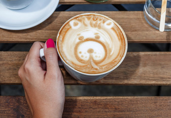 Female hands holding Latte art with bear shape, coffee cup