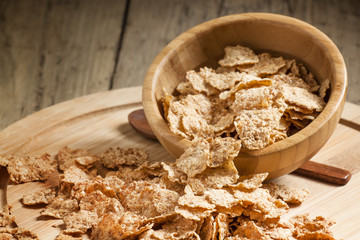 Wheat flakes poured from a wooden bowl, selective focus