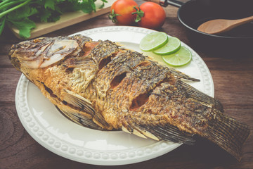 Fried fish on plate with vegetables and pan, filtered image