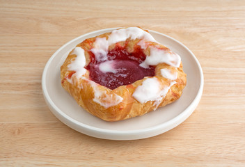 Raspberry danish on a small plate atop wood table top