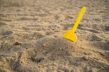 Fototapeta na wymiar Children's yellow shovel stuck in a pile of sand on the beach