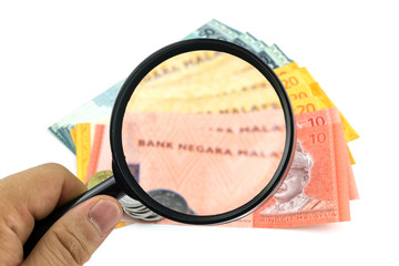 Hand holding magnifying glass looking at banknotes and coins on white background