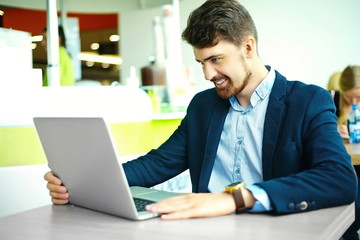 Fototapeta premium Young fashion smiling hipster man in the city cafe during lunch time with notebook in suit