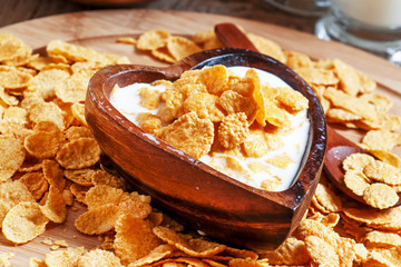 Corn flakes with milk in a wooden bowl in the shape of a heart,