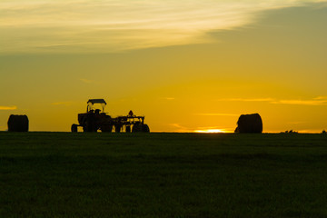 Naklejka premium Sunset with tractor and hay bales