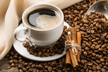 Close-up of coffee cup with roasted coffee beans on wooden background.