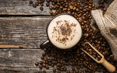 Close-up of coffee cup with roasted coffee beans on wooden background.