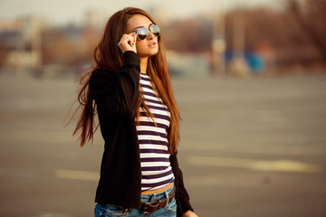 Outdoor fashion closeup portrait of nice pretty young hipster woman posing in sunglasses at sunset walks along the streets of the city.