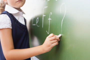 Schoolgirl writes English alphabet with chalk on blackboard