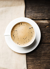 Close-up of coffee cup with roasted coffee beans on wooden background, view from the top