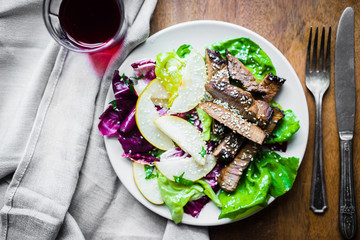 Sliced meat steak with green salad and pears