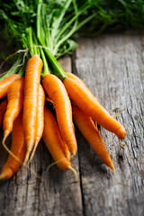 Raw carrot with green leaves on wooden background