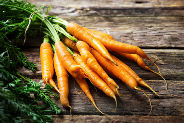 Raw carrot with green leaves on wooden background