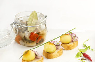 pickled herring in a glass jar with potato canapes