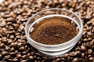 Fototapeta na wymiar Natural ground coffee heap in transparent glass bowl on сoffee grains background