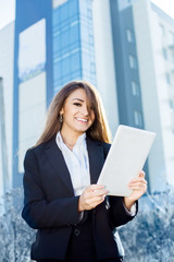 Successful businesswoman or entrepreneur using a digital tablet computer, standing in front of his office.