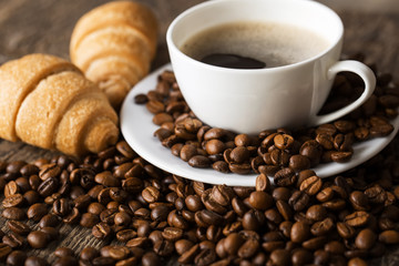 Close-up of coffee cup with roasted coffee beans on wooden background.