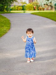 Portrait of a cute adorable little Asian girl child, one two years old, in blue dress and white shoes walking running in park outside on summer day, concept of first baby steps