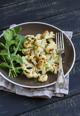 roasted cauliflower and fresh green salad on a brown plate on a dark wooden background