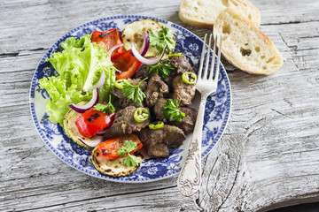 fried chicken livers, grilled vegetables and a fresh green salad on the blue plate on a light wooden background