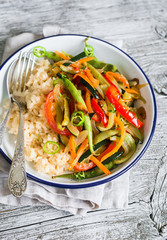 vegetable stir-fry and rice in an enamel plate on a light wooden background