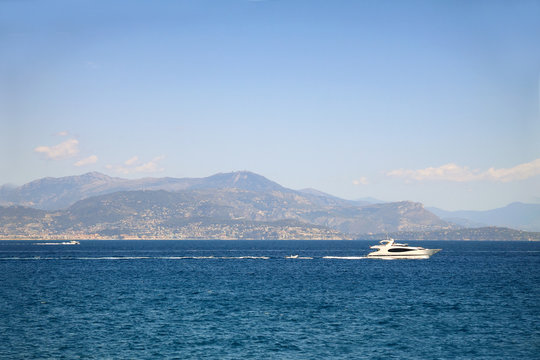 Seascape with mountains at the background and white yacht sailing in sea waters 