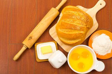 Loaf of bread, cheese, cracked eggs in a bowl and flour