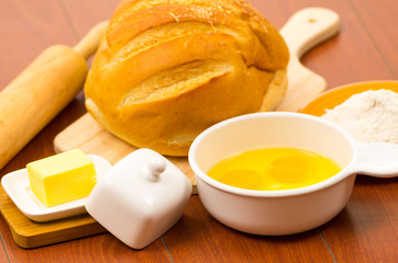 Loaf of bread, cheese, cracked eggs in a bowl and flour