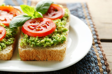 Vegan sandwich with avocado and vegetables on plate, on wooden background