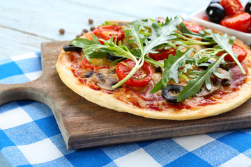Tasty pizza with vegetables and arugula on cutting board on table close up