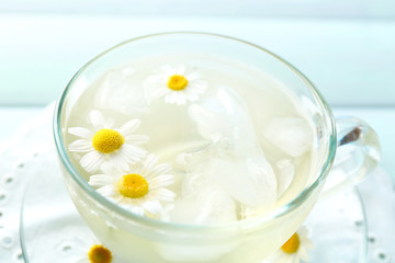 Glass of cold chamomile tea with ice cubes and chamomile flowers on color wooden background