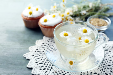 Cup of chamomile tea with chamomile flowers and tasty muffins on color wooden background